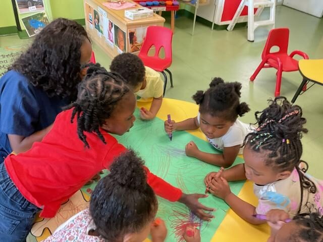 Children actively collaborate on a large green paper