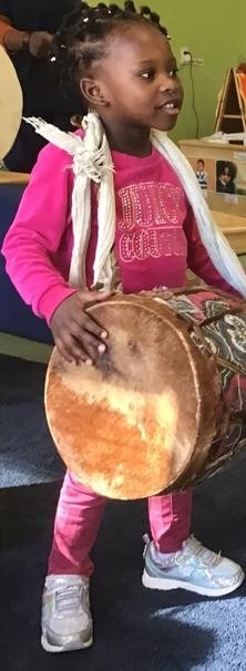 Young girl in a pink shirt and pink pants joyfully plays a drum