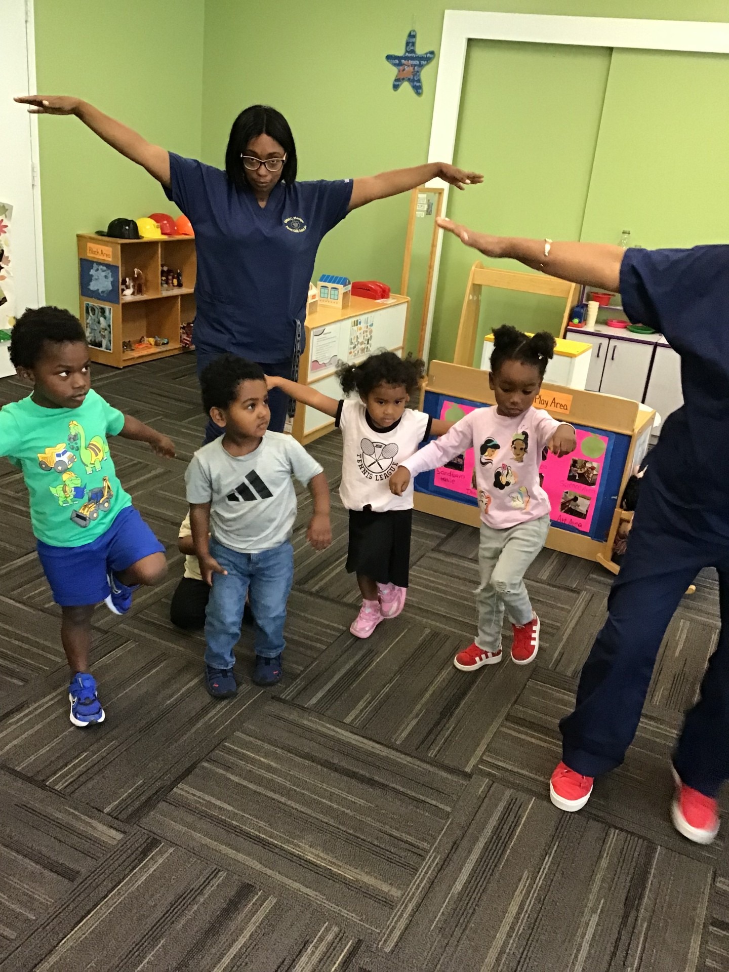 Children participate in a movement activity led by an adult in a colorful classroom