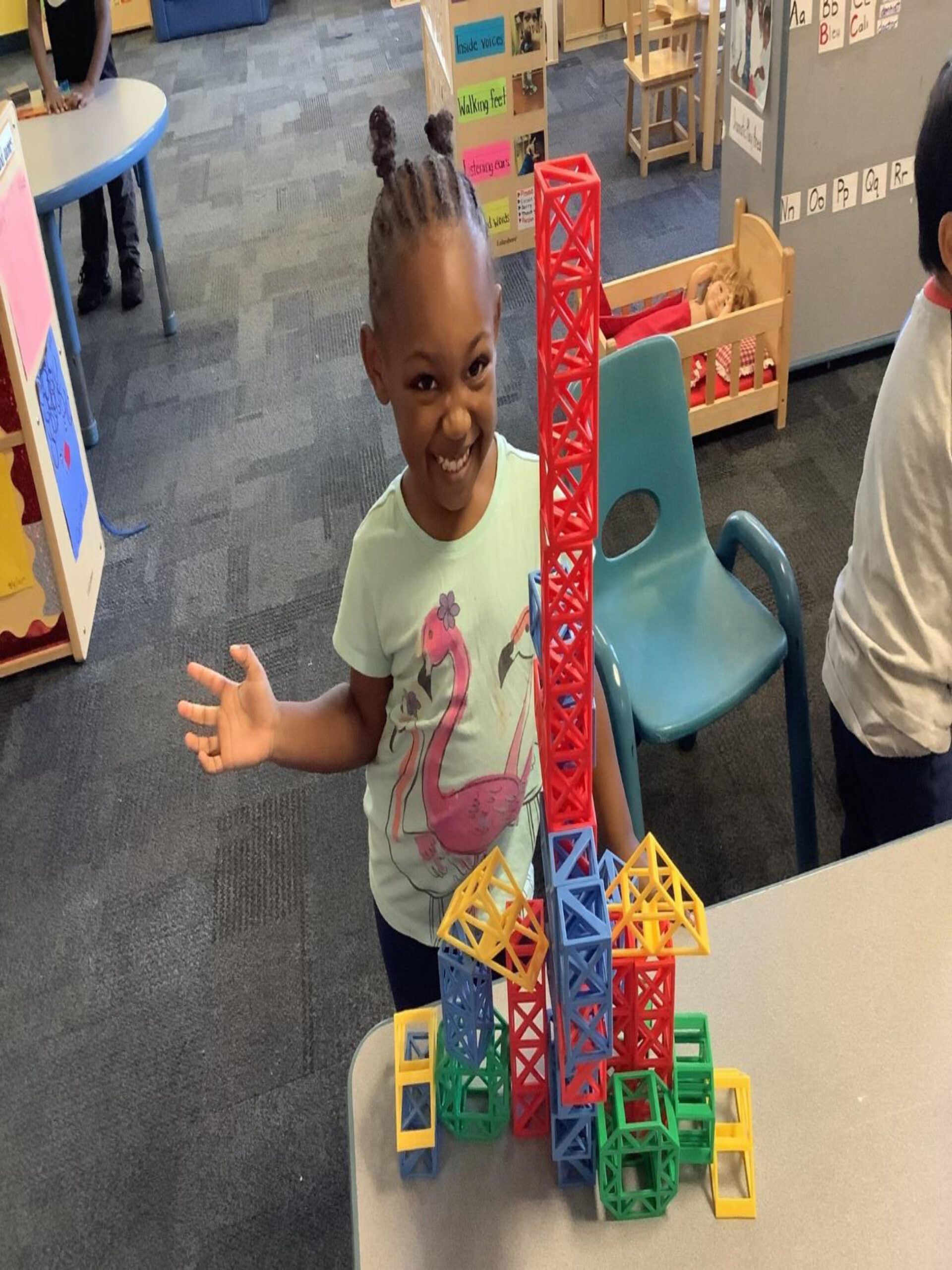 A smiling girl proudly displays a colorful structure made of building blocks,
