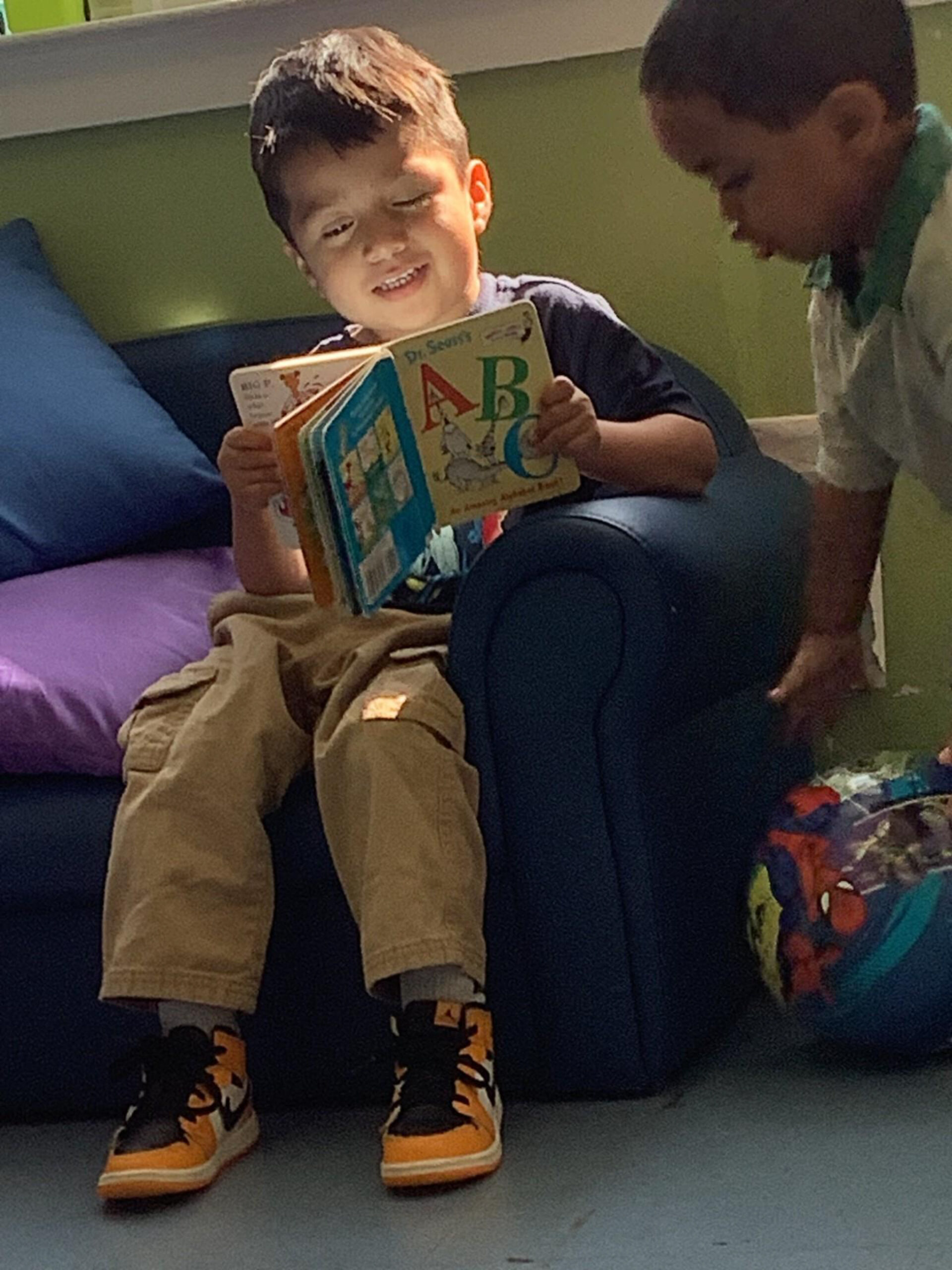 A smiling boy sits on a blue couch, reading a Dr. Seuss ABC book