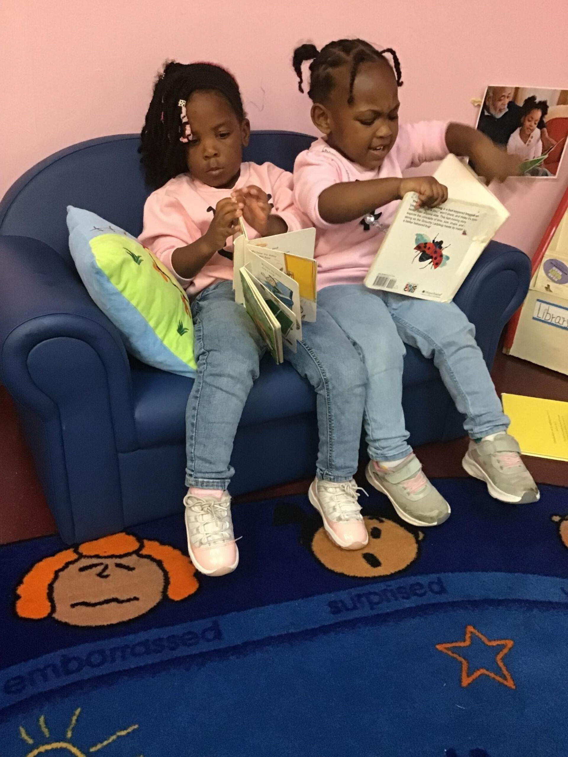 Two young girls in matching pink shirts sit together on a blue couch