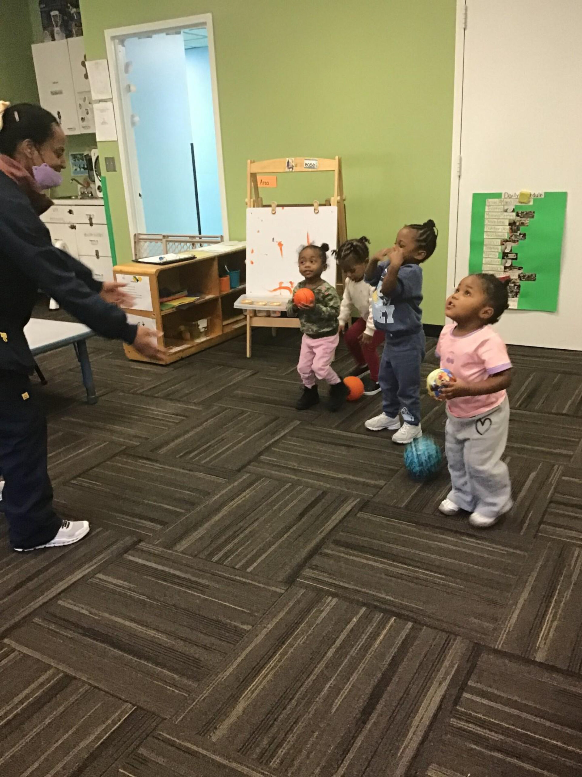 Children engage in a playful indoor activity, holding colorful balls, while an adult guides them in a lively learning environment.